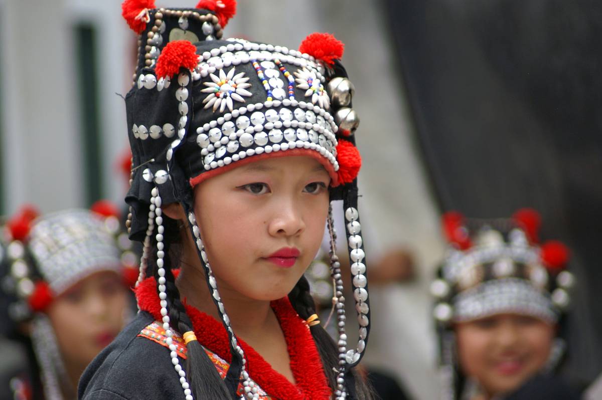 A woman trying on three different types of cultural event hair crowns in front of a mirror.